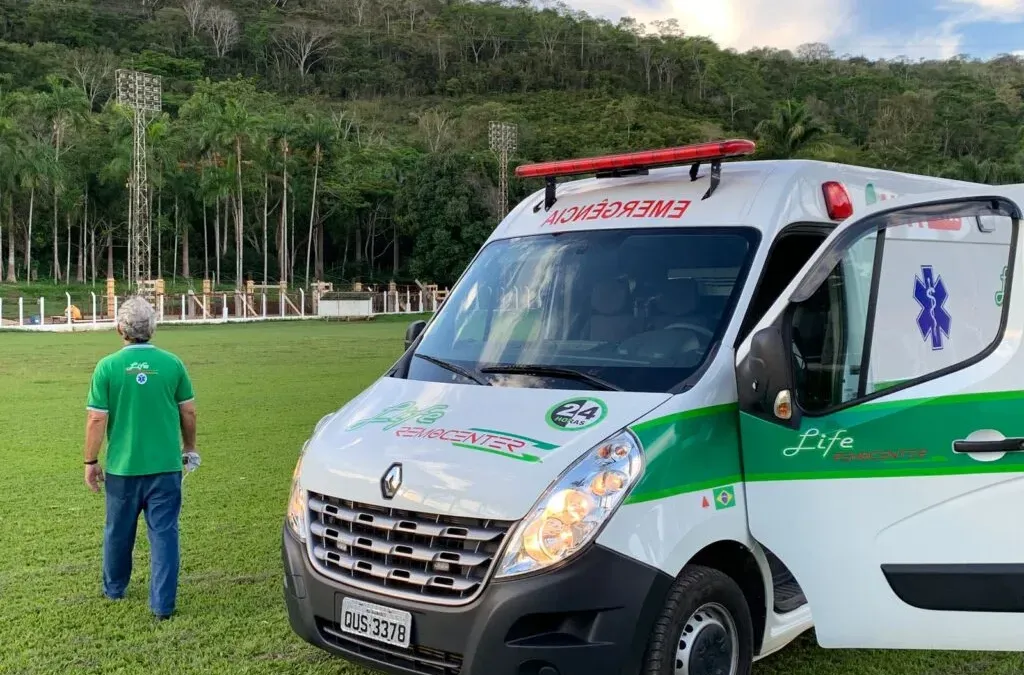 Ambulância da Life Remocenter estacionada em campo gramado, com socorrista uniformizado ao lado