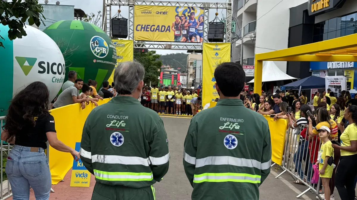 Condutor e enfermeiro da Life Remocenter de costas, observando a linha de chegada de uma corrida de rua cercada de público